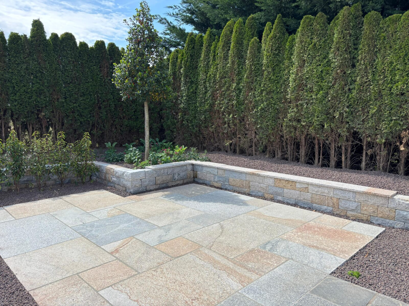 Gartensitzplatz mit grossformatigen Steinplatten und einer niedrigen Einfassungsmauer