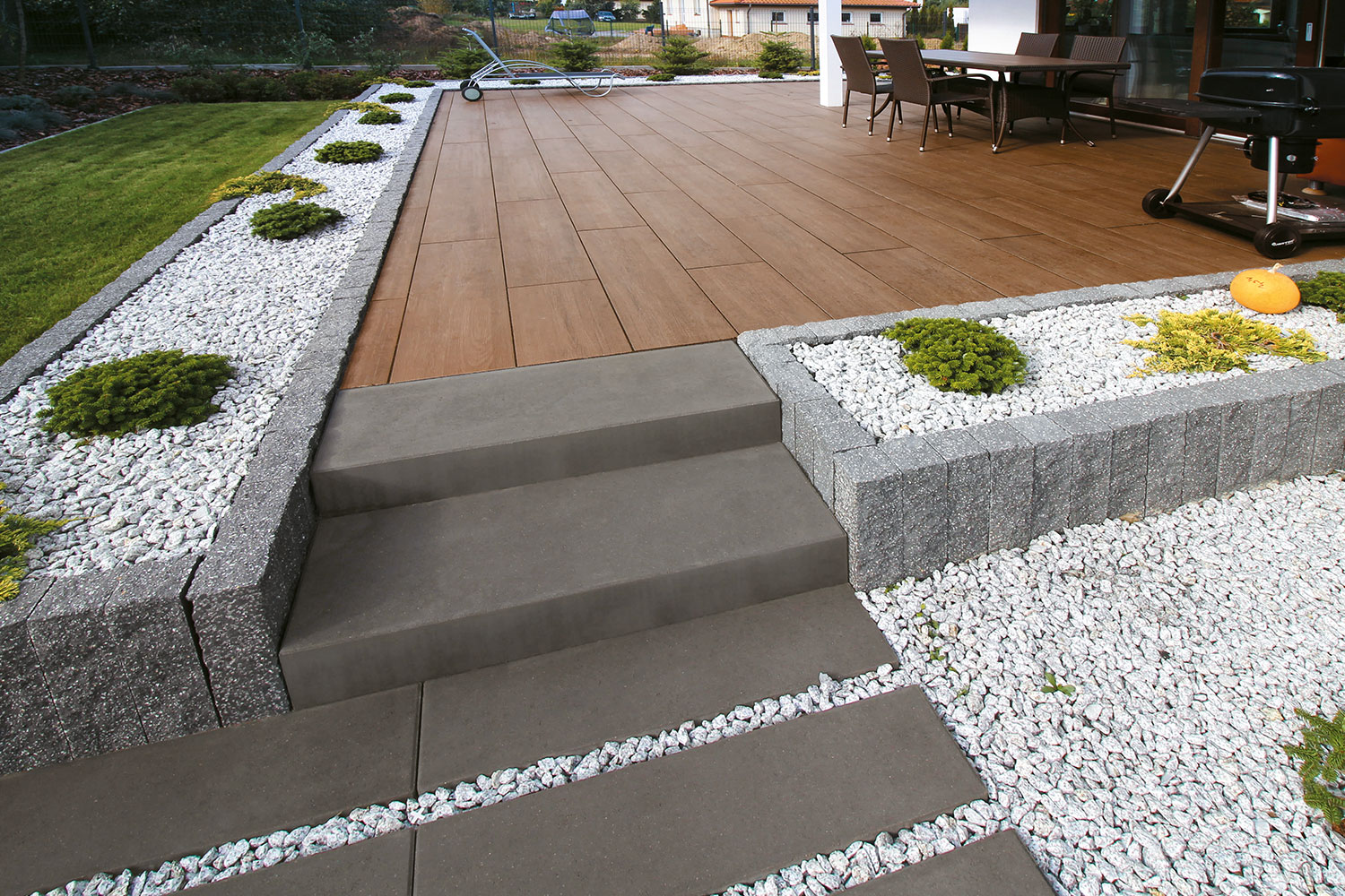 Terrasse mit braunen Platten in Holzoptik, grauen Treppenstufen und Kiesbeeten